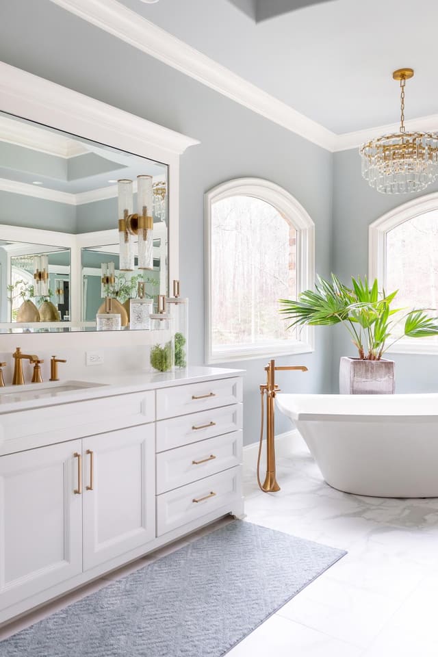 Master bathroom tub with Visual Comfort chandelier overtop, alongside white cabinetry.