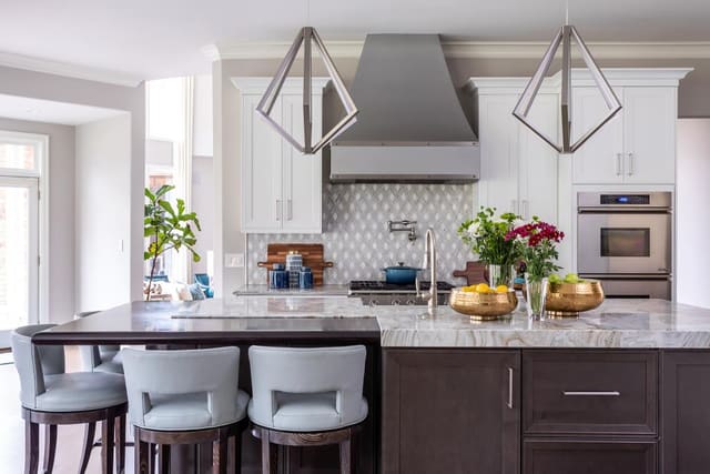 Kitchen with leather stools, silver lighting fixtures, and a marble countertop.