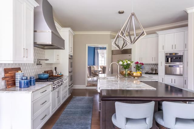 Kitchen with leather stools, silver lighting fixtures, and a marble countertop.