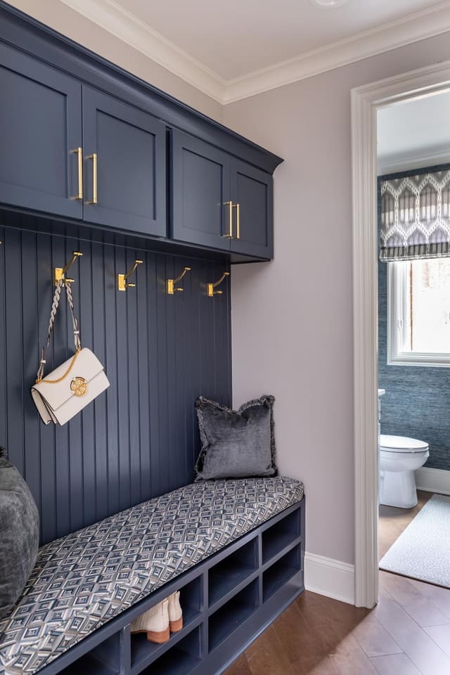 Navy painted mudroom with built in storage and an upholstered cushion.
