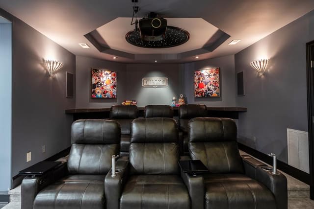 Theater room equipped with leather recliner seating and framed art.