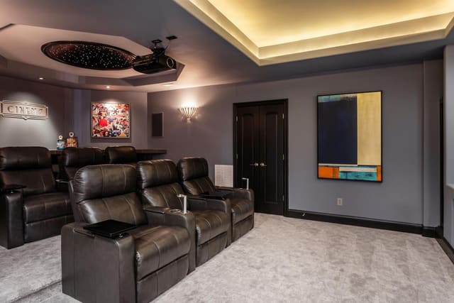 Theater room equipped with leather recliner seating and framed art.