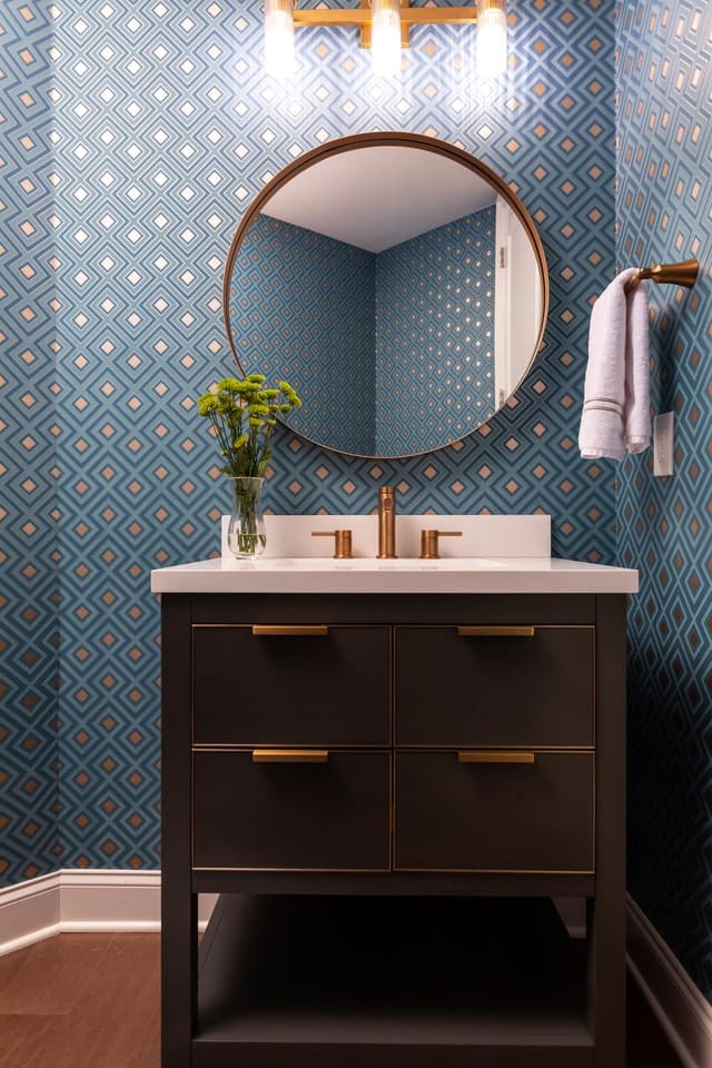 Powder bath with decorative cabinet, countertop, and patterned wallpaper.