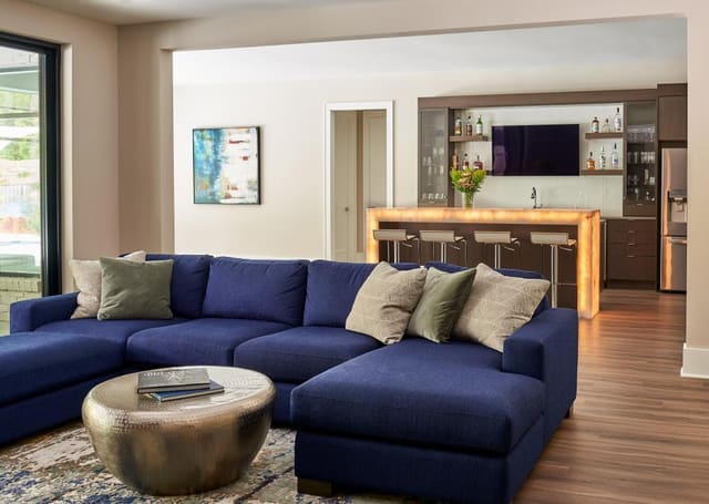 Entertainment room with navy sectional, antique nickel coffee table and modern rug, looking into Wine Room with back lit bar