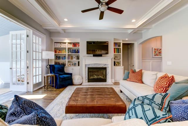 Family Room with 2 sofas, contrast throw pillows, large leather cocktail ottoman, blue velvet chair and neutral area rug.