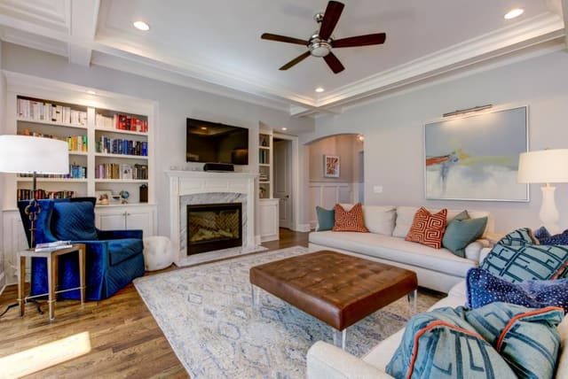 Family Room with 2 sofas, contrast throw pillows, large leather cocktail ottoman, blue velvet chair and neutral area rug.