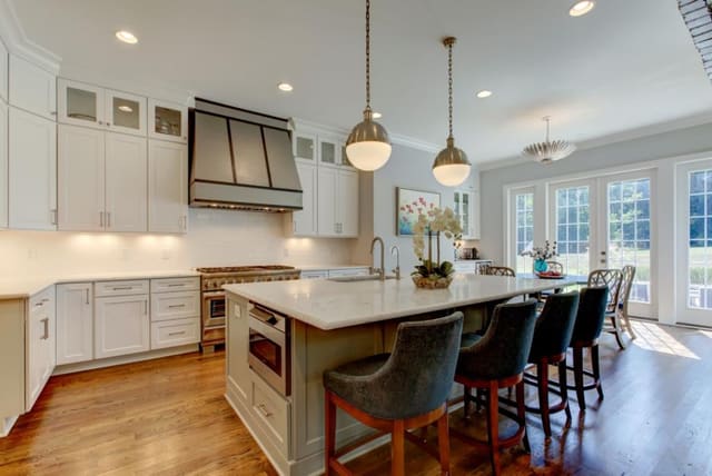 Kitchen with white cabinets, large island, globe pendants, custom metal hood, barstools