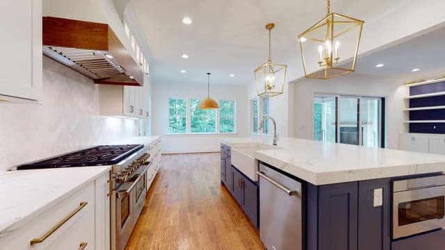 Kitchen with navy blue island, white cabinets, gold lantern pendant lighting, white tile backsplash, and white range hood with wood trim