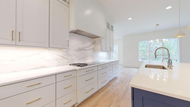 Kitchen with navy blue island, white countertops, white cabinets, white pendant lighting, white marble backsplash